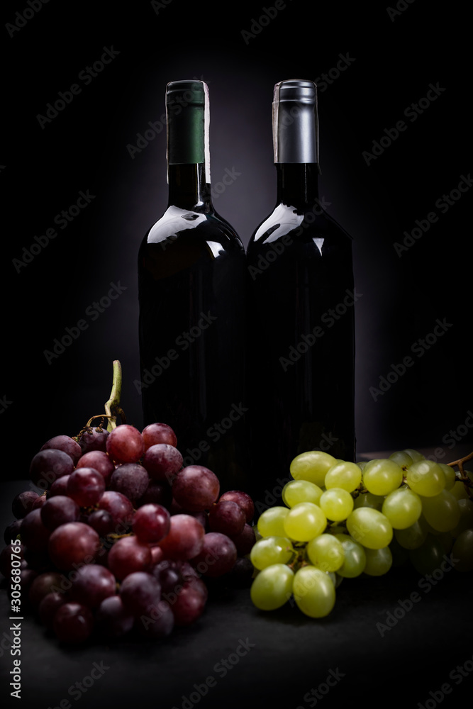 Two bunches of grapes on a dark background with two bottles of wine. A studio photo.