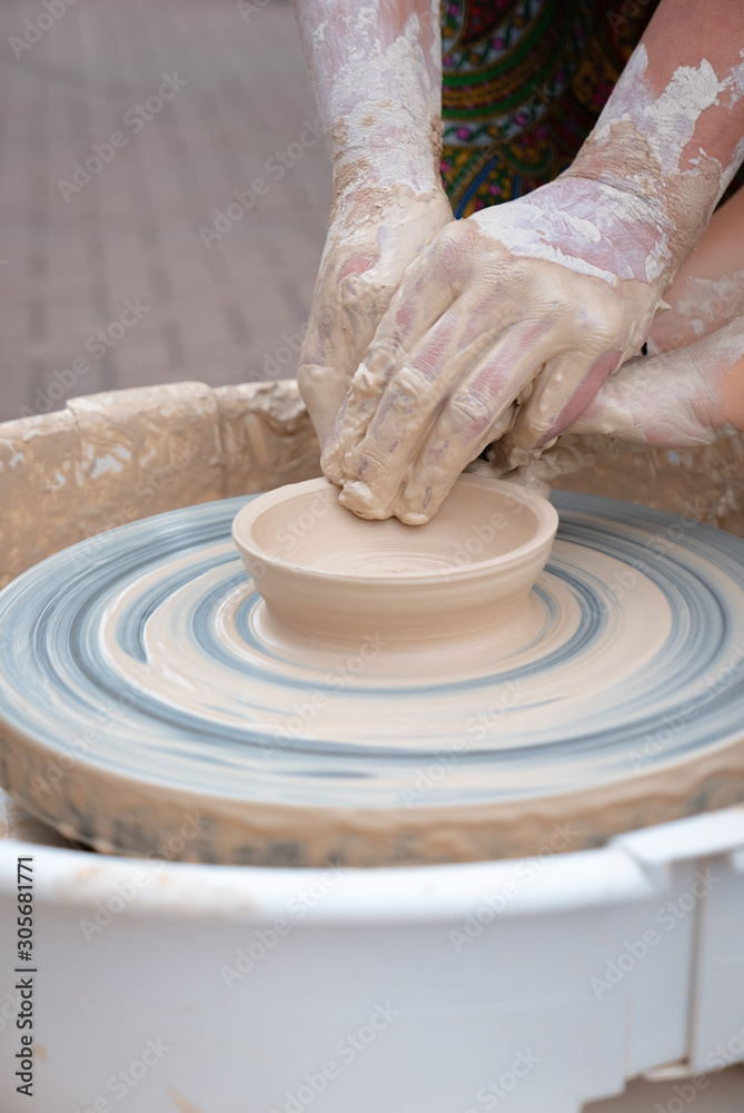 Hands forming clay on the pottery wheel