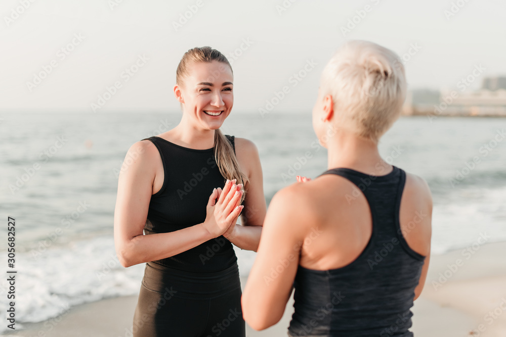 sporty woman smiling and laughing on the beach near ocean where she meditates together with mother sporty woman smiling and laughing on the beach near ocean where she meditates together with mother