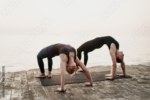 lesbian couple doing yoga exercises posing in asana together on the seaside