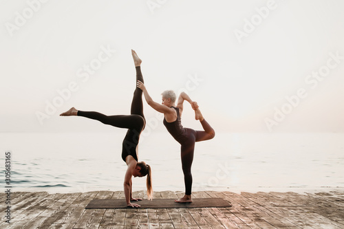 woman exercising acro yoga on the beach near sea in the morning with mature female tutor