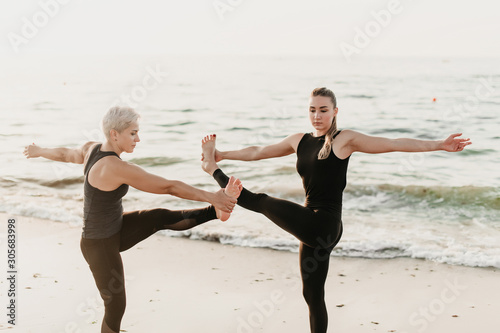 mother and daughter doing fitness yoga exercise on the beach near ocean in synchronization