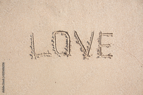Word LOVE drawn on the sand of sandy beach.