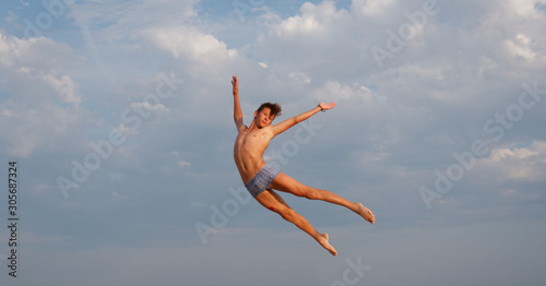athletic teenager on the beach in jump on the background of the sea and sky