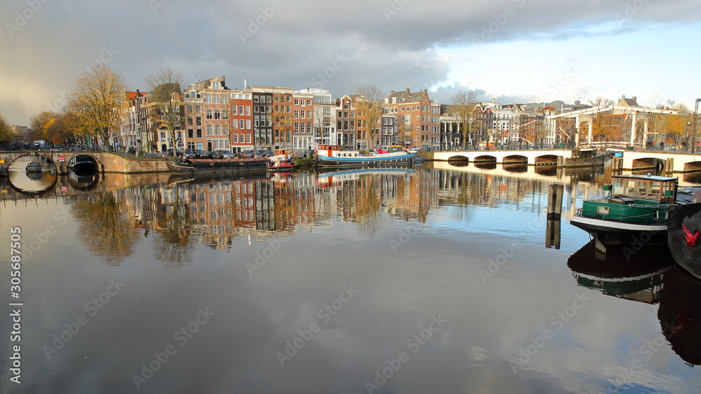 Reflections of colorful heritage buildings and houseboats, overlooking Amstel river with Skinny Bridge (Magere Brug) on the right, Amsterdam, Netherlands