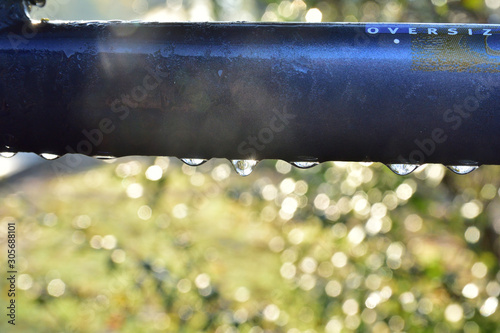 Fototapeta Naklejka Na Ścianę i Meble -  Rama rowerowa skąpana w kroplach rosy pod słońce w poranek, w tle bokeh na kroplach wody.