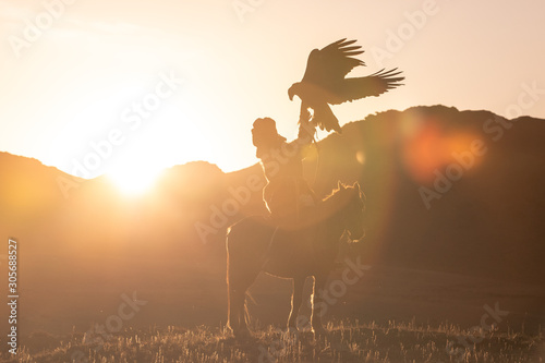 Traditional kazakh eagle hunter posing with his golden eagle on horseback at sunset. Ulgii, Mongolia.