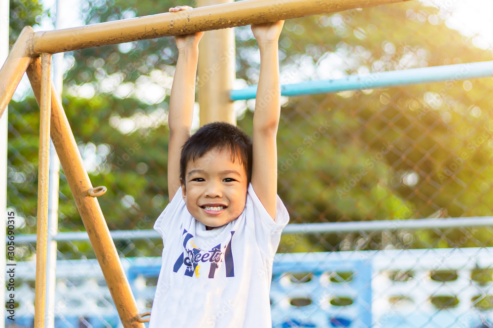 Fototapeta premium Kid exercise for health and sport concept. Happy Asian child boy playing and hanging from a steel bar at the playground. 5 years old.