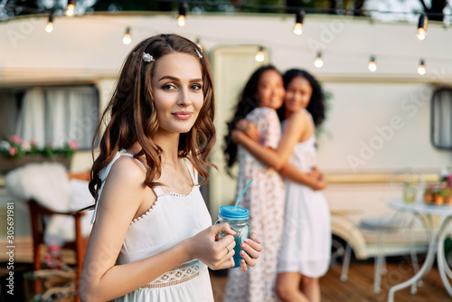 Beautiful young woman portrait during picnic beside her camper van and friends on background
