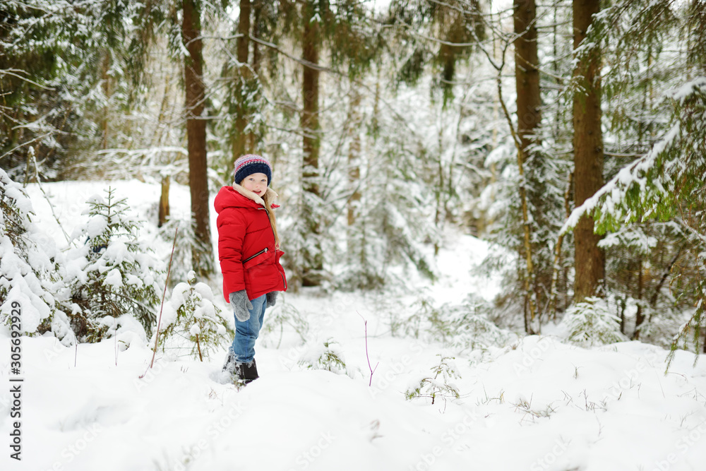 Adorable little girl having fun in beautiful winter forest. Happy child playing in a snow.