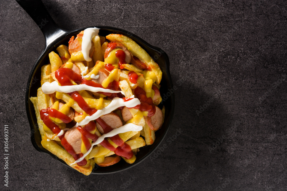 Typical Latin America Salchipapa. Sausages with fries, ketchup, mustard and mayo in iron pan and black background. Top view. Copy space