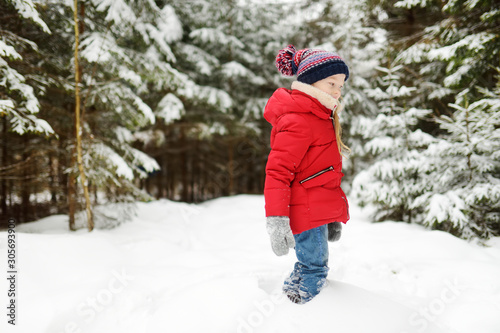 Adorable little girl having fun in beautiful winter forest. Happy child playing in a snow.