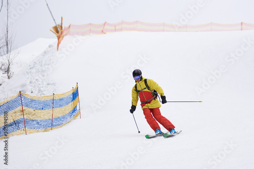 Young guy skier backpacker descending downhill on skis. Ski slopes obstructed with net for safe sports, skiing, training carve turn technique. Safety skiing at ski resort. White background. Front view