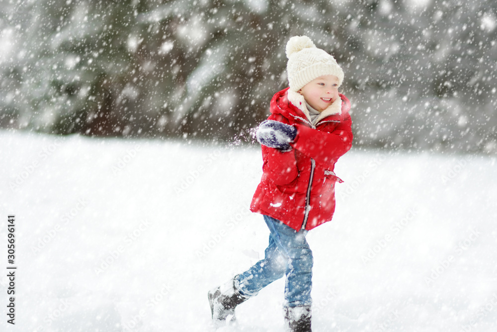 Adorable young girl having fun in beautiful winter park during snowfall. Cute child playing in a snow.