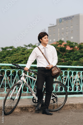 Fototapeta Naklejka Na Ścianę i Meble -  Full length portrait of a student talking on phone and standing by a bike isolated on white background