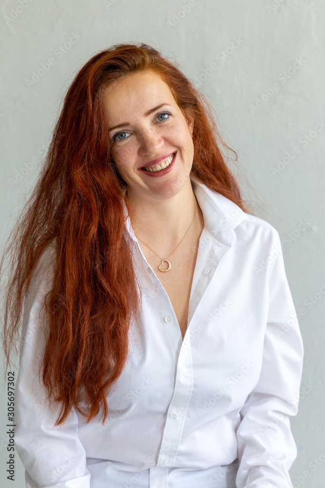 Portrait of beautiful red-haired woman wearing white shirt and smiling friendly and openly Portrait of beautiful red-haired woman wearing white shirt and smiling friendly and openly