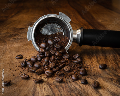 Coffee beans and ground coffee spilling out of a coffee filter holder on a wooden table.
