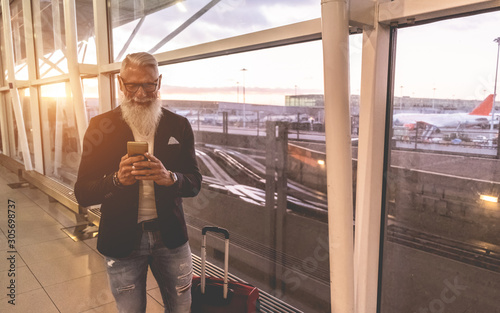 Senior trendy man using smartphone inside international airport - Soft focus on his face photo