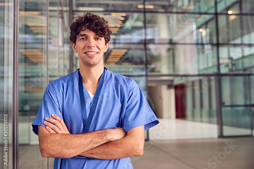 Portrait Of Young Male Doctor Wearing Scrubs Standing In Modern Hospital Building photo