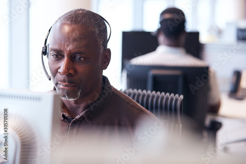 Mature Businessman Wearing Telephone Headset Talking To Caller In Customer Services Department photo