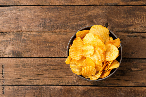 Fotografija Tasty potato chips in bowl on rustic wooden background with copyspace
