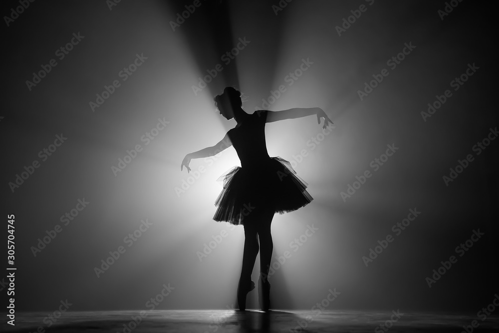 Profesjonalny balerina taniec balet w reflektorach dymu na dużej scenie. Piękna młoda dziewczyna ubrana w czarną sukienkę tutu na tle reflektorów. Czarny i biały. <span>plik: #305704745 | autor: kohanova1991</span>
