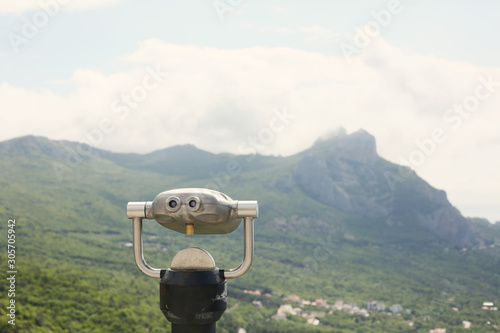 Stationary anti vandal metal binoculars with the background of mountain and sea landscape on a summer sunny day.Telescope. Copy space for text. Exploring the world and tourism concept. Crimea,Russia. 