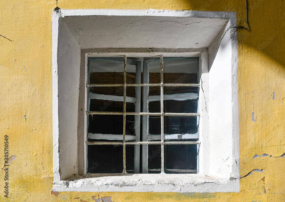 Close-up of the small, square window of an abandoned house with yellow wall background, Italy