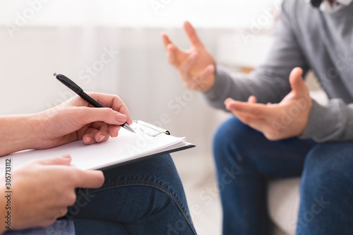Psychotherapist writing notes, giving diagnosis to emotional man photo