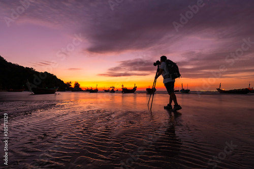 Silhouette of photographer taking a photo by using DSLR camera on tripod on the beach with sunset © sutthichai