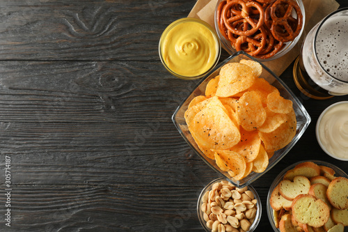 Beer snacks, glass of beer, potato chips, beer nuts, sauces, glass of beer on wooden background, space for text. Top view