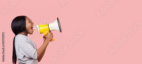 Young woman shouting in megaphone over pink background photo