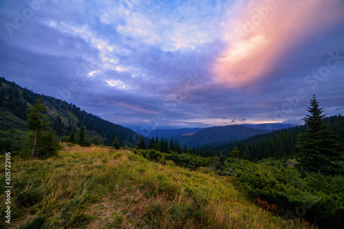 Beautiful sunset in mountains panorama, evening with colorful clouds and fir trees forrest scene. Autumn background. Trekking and hiking summer travel nature landscape background.