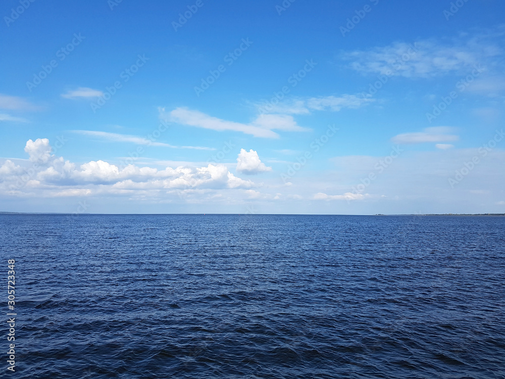 Dark blue sea and sky in the clouds. Bright blue sky with white clouds and calm shining surface of the water in the sea background.