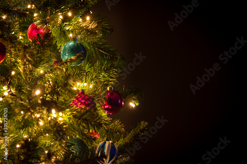 Closeup of Christmas tree with lights, balls and decorations, dark background