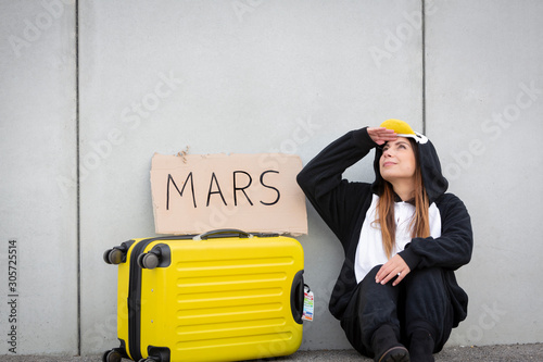 Young woman, with penguin costume and yellow suitcase, has to travel due to global warming. Symbolizes a sad penguin who has to leave his homeland because of global warming or climate change. photo