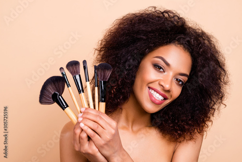 Close up photo beautiful she her dark skin model lady brunette wavy hairdo aesthetic look toothy mouth make maquillage show new professional brushes wear nothing isolated pastel beige background photo