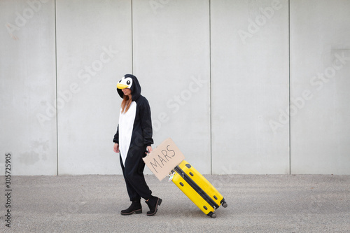 Young woman, with penguin costume and yellow suitcase, has to travel due to global warming. Symbolizes a sad penguin who has to leave his homeland because of global warming or climate change. photo