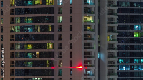 Rows of glowing windows with people in apartment building at night.