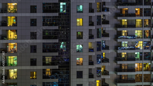 Rows of glowing windows with people in apartment building at night.