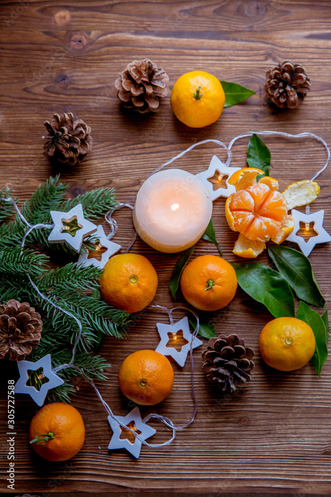 Christmas and new year decor. Christmas card. Tangerines, candle, lights, cones on a wooden background Christmas and new year decor. Christmas card. Tangerines, candle, lights, cones on a wooden background