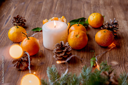 Christmas and new year decor. Christmas card. Tangerines, candle, lights, cones on a wooden background