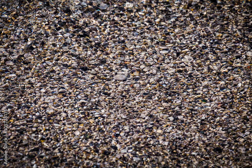 Background of multicolored sea pebbles on the beach under water. Small color wet stones gravel texture background. Background of multicolored sea pebbles on the beach under water. Small color wet stones gravel texture background.