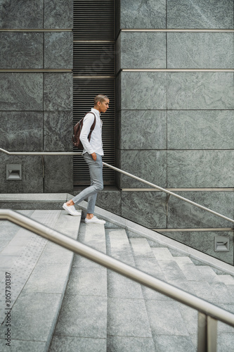 Young man dressed in casual clothes and backpack in the city center comes down the stairs - Millennial is going to work