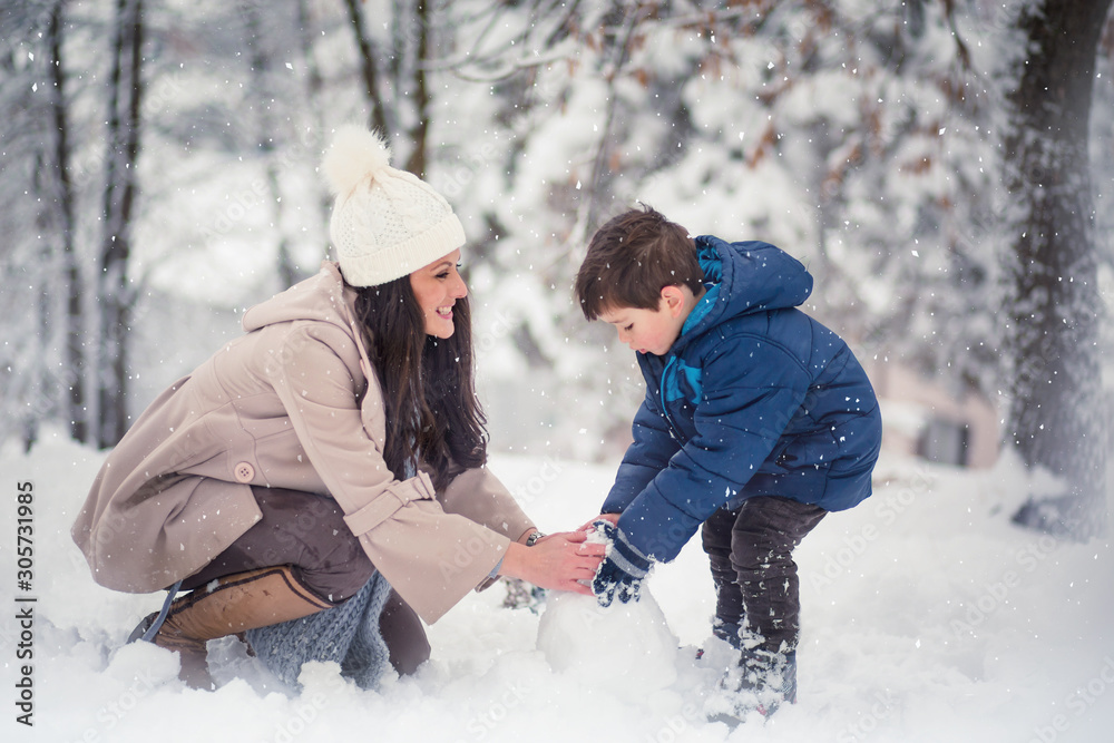 Young, beautiful mom and her cute little boy playing in the snow, enjoying winter