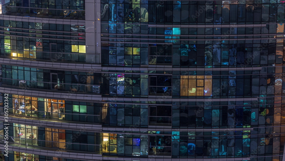 Rows of glowing windows with people in apartment building at night.