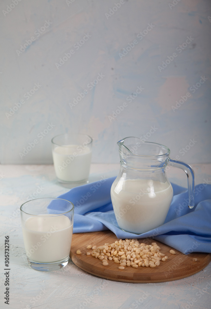 Vegetarian pine nut milk in glass cups and jug, on white background. Vertikal Vegetarian pine nut milk in glass cups and jug, on white background. Vertikal