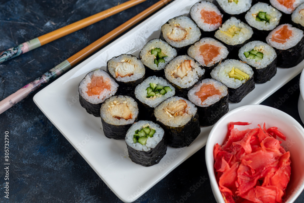 Sushi with fish, with cucumber, with eel, with avocado. Wrapped in Nori Seaweed. Food for vegetarians. Soy sauce, ginger, wasabi in white bowls. Copy space. Sushi with fish, with cucumber, with eel, with avocado. Wrapped in Nori Seaweed. Food for vegetarians. Soy sauce, ginger, wasabi in white bowls. Copy space.