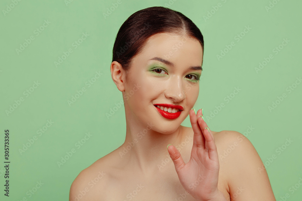 Portrait of beautiful woman with bright make-up, red eyewear and hat on green studio background. Stylish and fashionable make, hairstyle. Beauty, fashion and ad concept. Whispering secrets, sales. Portrait of beautiful woman with bright make-up, red eyewear and hat on green studio background. Stylish and fashionable make, hairstyle. Beauty, fashion and ad concept. Whispering secrets, sales.