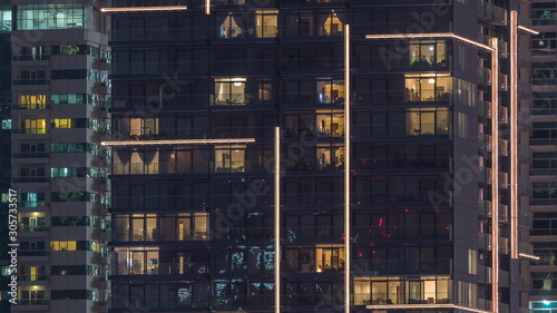 Rows of glowing windows with people in apartment building at night.